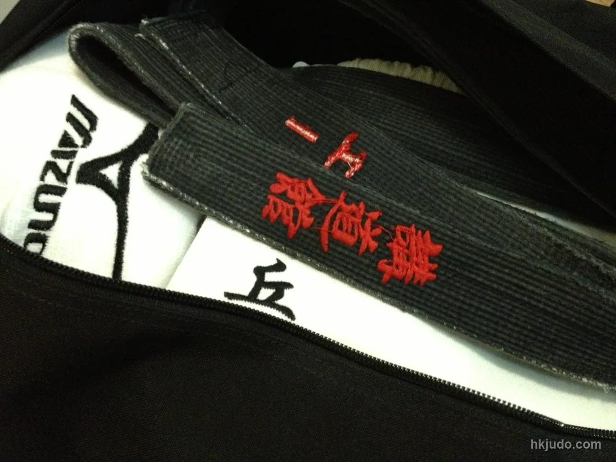 Close-up of a black dan belt and a white judo gi, the belt carrying embroidered characters, resting on a black carry bag